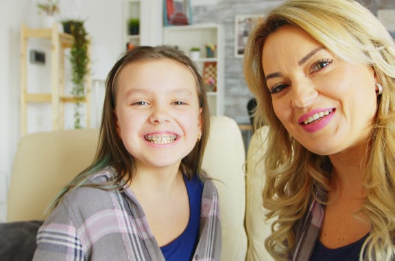 a mother and her daughter smiling - the daughter is wearing dental braces